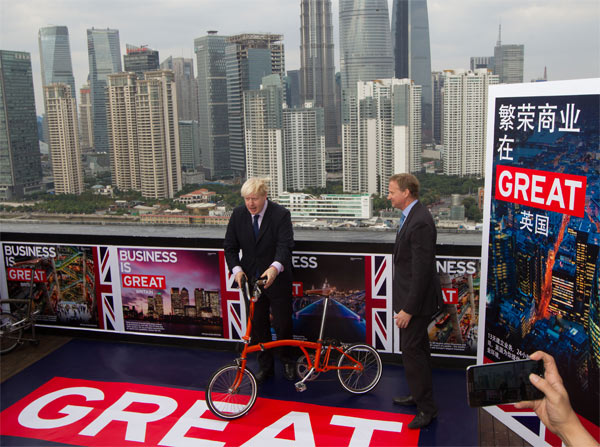 Mayor of London Boris Johnson (left) poses with a fold-up bicyle on a 30th-floor balcony overlooking the Bund in Shanghai on Wednesday. Johnson came to China to promote trade, investment and products from Britain. Gao Erqiang / China Daily London mayor hails free trade, subway system on China tour