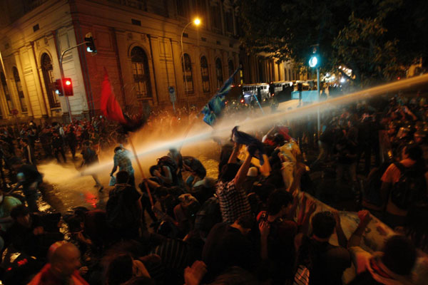 Demonstrators are hit by a jet of water released from a riot police vehicle during a protest in Santiago Oct 20, 2011. Chile students storm Senate building